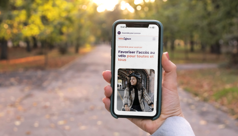 Main tenant un téléphone mobile sur lequel est affiché le site de Vélo-Égaux